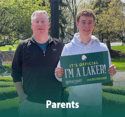 A dad posing with his son who has decided to attend AV. The son holds a poster reading "It's Official. I'm a Laker!"